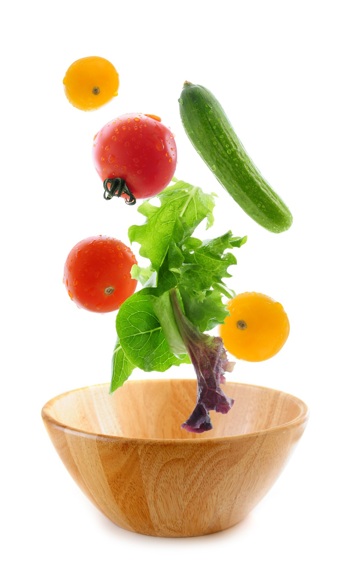 Assorted fresh vegetables falling into a wooden salad bowl isolated on white background